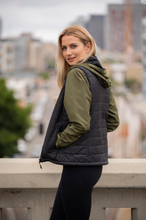 Load image into Gallery viewer, Woman standing sideways against a bridge railing wearing our Womens Lightweight Black Puffer Vest
